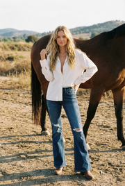 Woman in a white shirt and blue jeans standing next to a horse in an outdoor setting